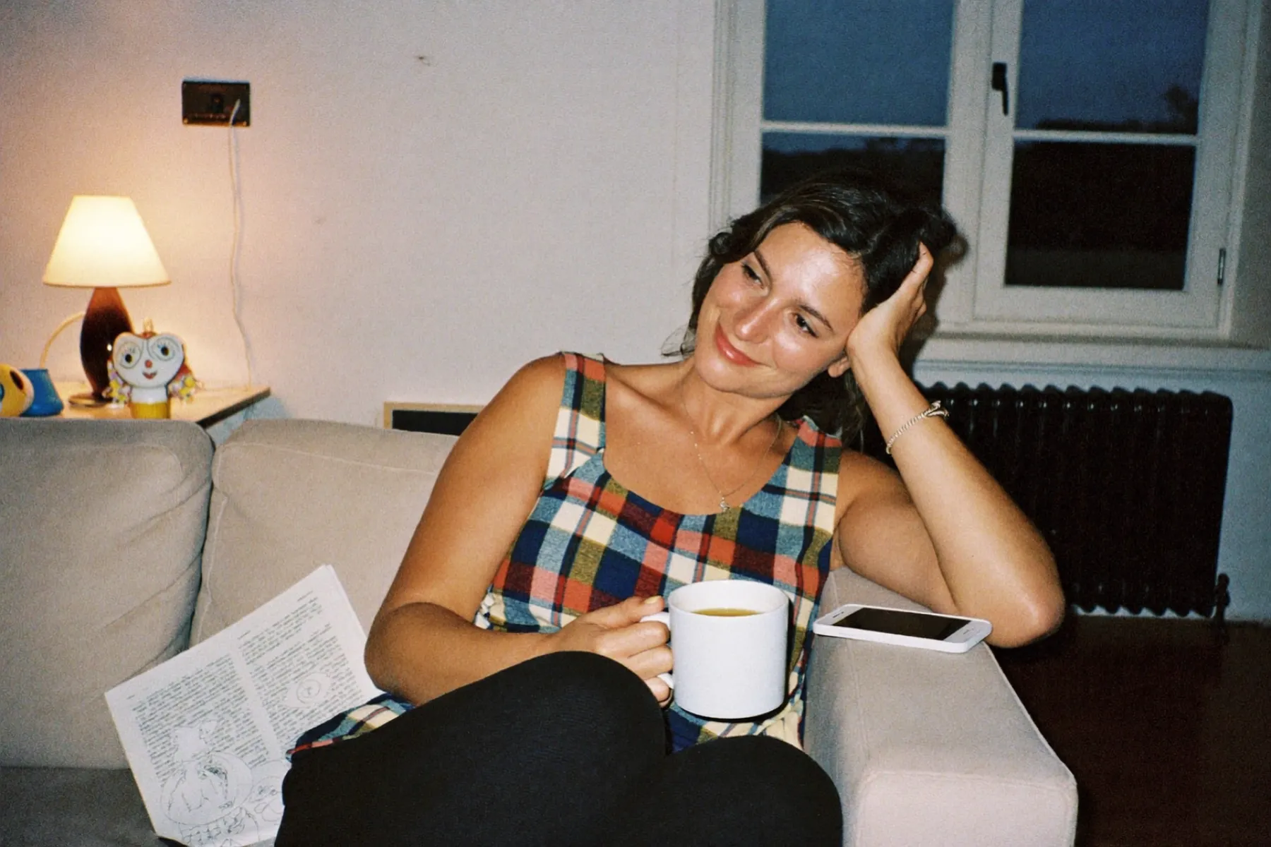 With the children asleep, a mum relaxes on the sofa with a mug of tea, her phone put down beside her.