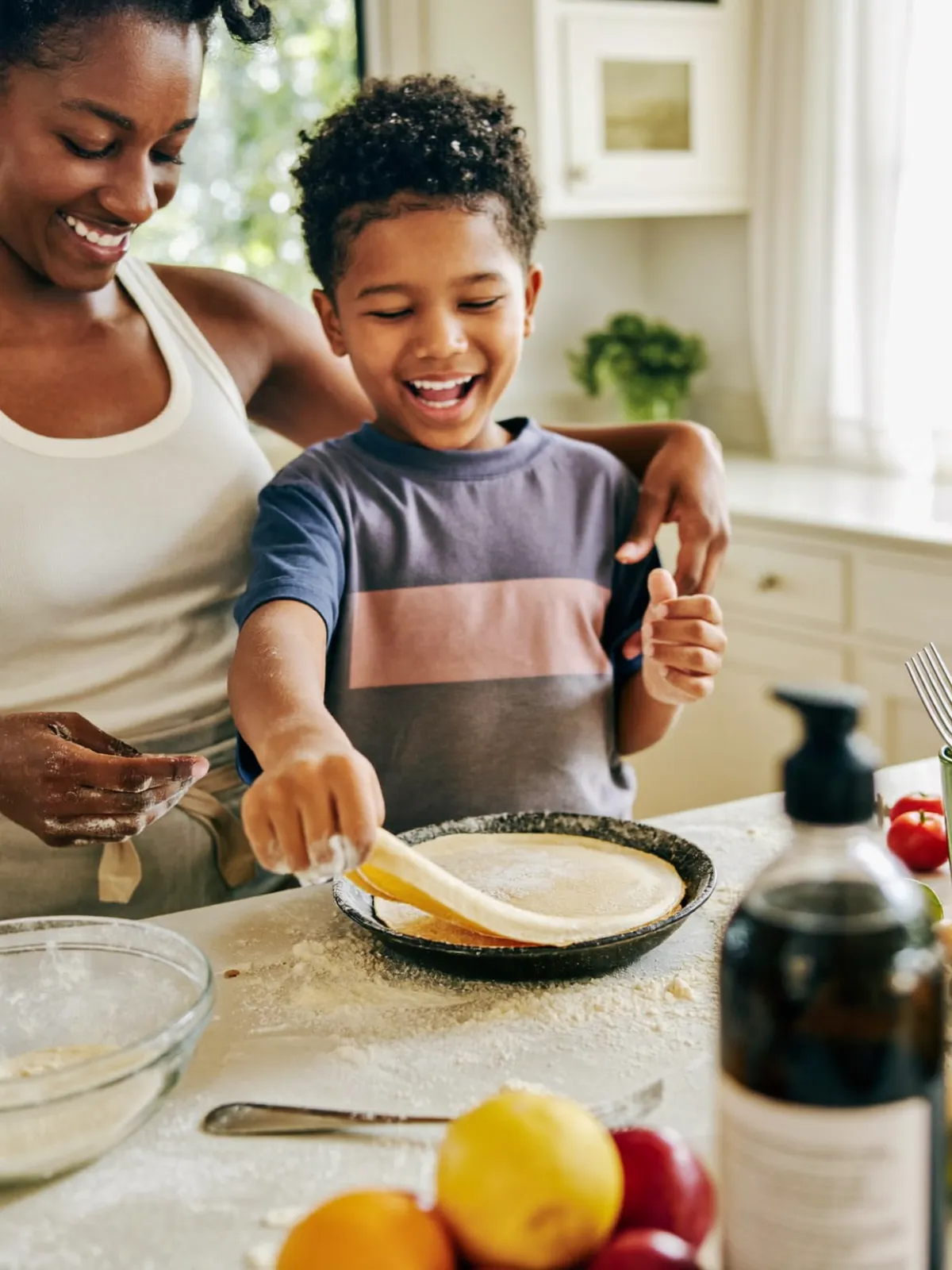 A mum and her son laughing as he flips a pancake at the kitchen counter on a Saturday morning.